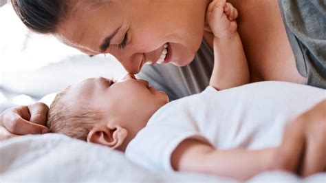 mama su kūdikiu, nešamu slinge, tarp žydinčių gėlių